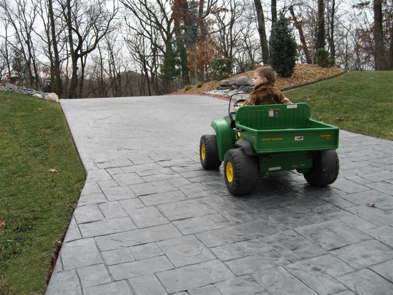 child driving toy car on a stamped concrete driveway